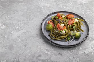 Tagliatelle green spinach pasta with tomato, pea and microgreen sprouts on a gray concrete