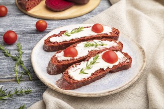 Red beet bread sandwiches with cream cheese and tomatoes on gray wooden background and linen