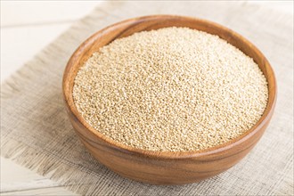 Wooden bowl with raw white quinoa seeds on a white wooden background and linen textile. Side view,