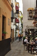 Narrow alley with restaurants, pedestrians, tourists in the historic centre of Seville, Spain,