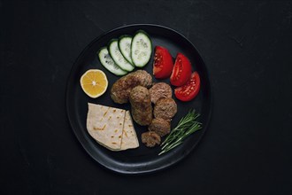 Traditional Cypriot Seftalia dish, grilled, with vegetables, pita, and sauce, top view, on a black