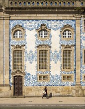 Woman passes by the facade of Igreja do Carmo church, adorned with intricate blue and white tiles,