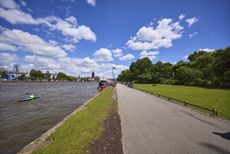 Riverside promenade and Main with canoeists under a blue sky with cumulus clouds in Frankfurt am