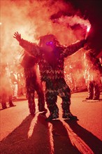 Person in an illuminated costume standing in the smoke at a night-time celebration, carnival,