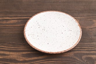 Empty white with dots ceramic plate on brown wooden background. Side view, copy space