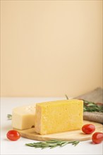 Various types of cheese with rosemary and tomatoes on wooden board on a white and orange background