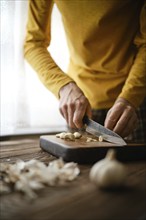 Unrecognizable man chopping garlic on wooden cutting board