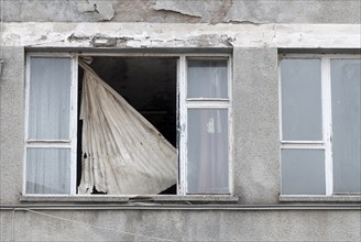 A damaged window with a torn blind in a decaying building, facade, crumbling paint, crumbling