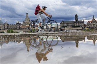 The Dresden silhouette with a cyclist and dark clouds behind the Church of Our Lady is reflected in