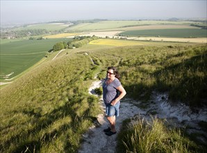 Woman walking up steep chalk scarp slope onto downland Cherhill, Wiltshire, England, UK