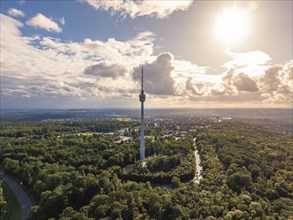 The television tower rises above a vast wooded area as the sun breaks through the clouds,