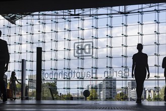 Central station, travellers in front of the glass facade with the logo of Deutsche Bahn AG. Berlin,