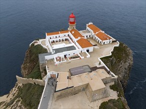 A red lighthouse on a rock above the ocean with several white buildings giving a calm feeling,