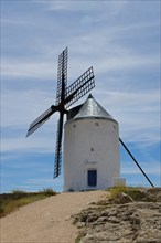 An old windmill under a blue sky with clouds at the end of a dirt road in a rural landscape,