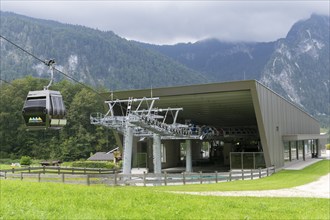 Cable car of the Jennerbahn at the valley station, surrounded by green meadows and wooded mountains