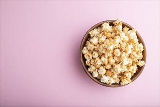 Popcorn with caramel in wooden bowl on a pastel pink background. Top view, flat lay, copy space