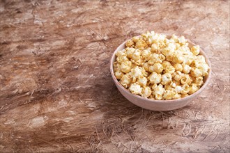 Popcorn with caramel in ceramic bowl on brown concrete background. Side view, copy space