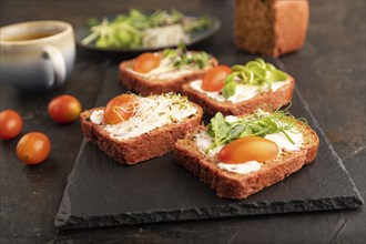 Red beet bread sandwiches with cream cheese, tomatoes and microgreen on black concrete background.