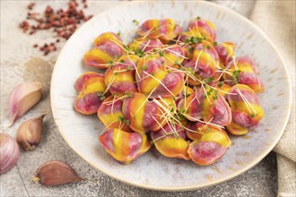 Rainbow colored dumplings with pepper, herbs, microgreen on brown concrete background and linen