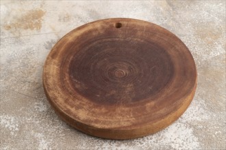 Empty round wooden cutting board on brown concrete background. Side view, close up