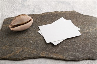 White paper business card, mockup with natural stone and seashell on gray concrete background.