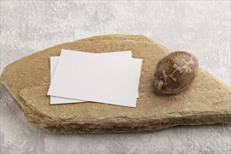 White paper business card, mockup with natural stone and seashell on gray concrete background.