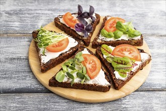 Grain rye bread sandwiches with cream cheese, tomatoes and microgreen on gray wooden background.