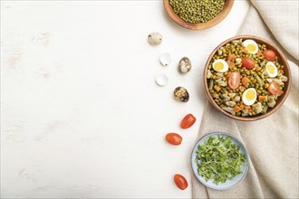 Mung bean porridge with quail eggs, tomatoes and microgreen sprouts on a white wooden background