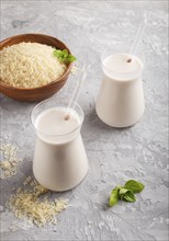 Organic non dairy rice milk in glass and wooden plate with rice seeds on a gray concrete background