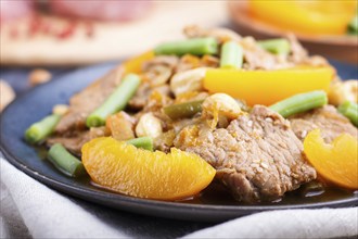 Fried pork with peaches, cashew and green beans on a black concrete background. Side view, close