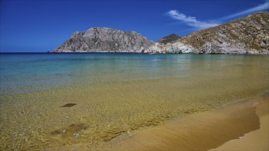 Beach with clear water and a golden sandy beach surrounded by rocks and a blue sky, Psili Ammos