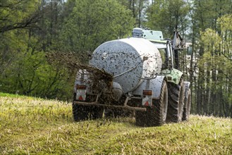 Slurry is spread on a field with a tractor from a slurry tanker to fertilise the farmland, North