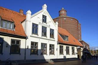 A white traditional building with a tiled roof in the foreground in front of an unusual round tower