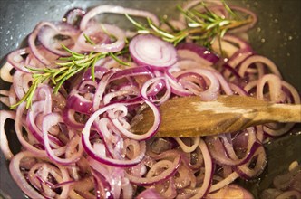 Close up onion rings cooking in wok pan with rosemary wooden stirrer