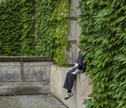 A person sits on the windowsill, covered by ivy on the house facade, Berlin, Germany, Europe