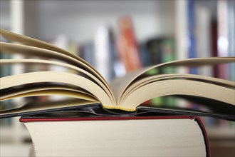 Close-up of an open book, behind it a blurred bookshelf