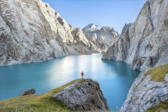 Young man at the turquoise mountain lake Kol Suu with rocky steep mountains, Kol Suu Lake, Sary