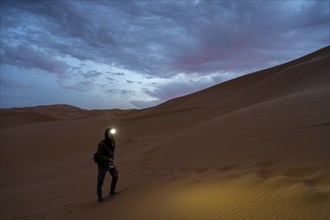 Photographer with headlamp at sunrise in the desert, dunes, Erg Chebbi, Sahara, Merzouga, Morocco,