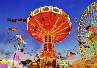 The colourfully illuminated Wellenflug chain carousel and the Ferris wheel in the evening, Cranger