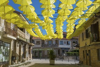 Street full of yellow umbrellas forming an artistic shadow installation under a blue sky and old