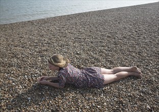 Model released young teenage girl wearing floral dress lies on shingle beach near the sea