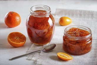 Tangerine and kumquat jam in a glass jar with fresh fruits on white background. Homemade, close up