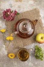 Red tea with herbs in glass teapot on brown concrete background and linen textile. Healthy drink