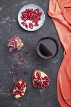 Glass of pomegranate juice on a black concrete background with red textile. Top view, close up,