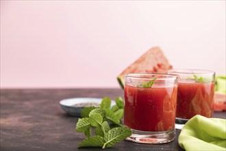 Watermelon juice with chia seeds and mint in glass on a black and pink background with green