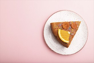 A piece of orange cake on a pastel pink background. Top view, flat lay, copy space