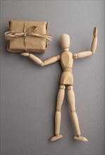 Wooden mannequin holding a gift box on gray pastel background. close up, isolated, delivery concept