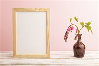 Wooden frame with pink dicentra, broken heart in ceramic vase on pink pastel background. side view,