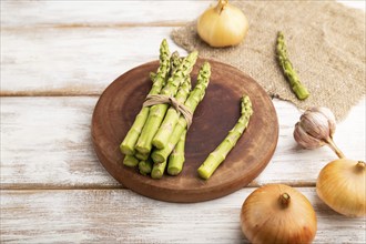 Bunch of fresh green asparagus, garlic, onion on white wooden background. Side view, close up.