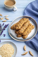 Crumble cookies with seasme and almonds on ceramic plate with cup of coffee and blue linen textile